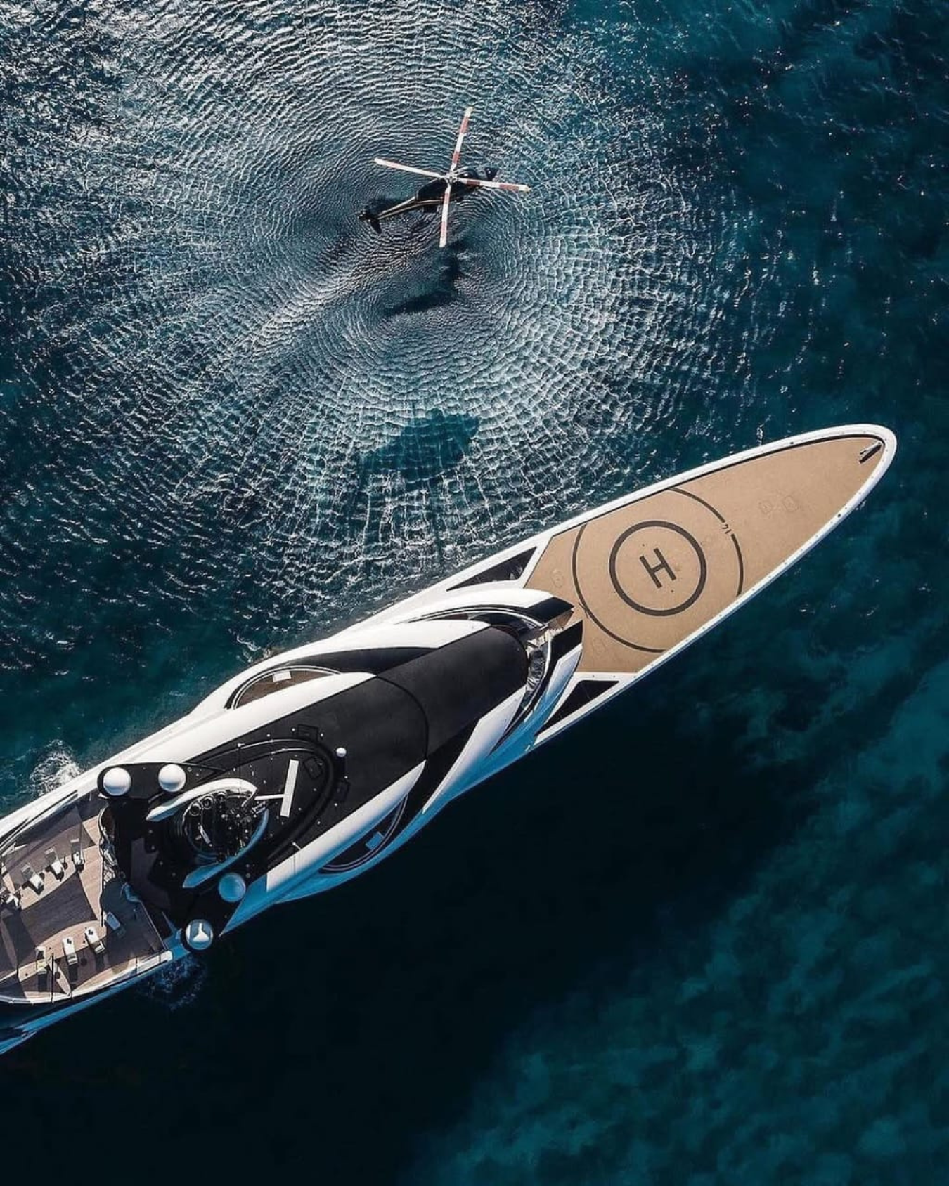 Aerial view of a superyacht at sea with a helicopter landing on its helipad